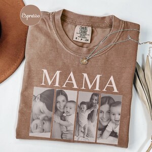 May include: An espresso-colored t-shirt featuring the word MAMA in large white capital letters above a collage of four black and white photographs showing a parent and child. A silver-toned necklace with a small circular pendant rests on the neckline.