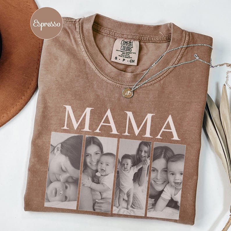 May include: An espresso-colored t-shirt featuring the word MAMA in large white capital letters above a collage of four black and white photographs showing a parent and child. A silver-toned necklace with a small circular pendant rests on the neckline.