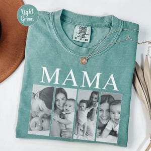 May include: A light green t-shirt featuring the word MAMA in white capital letters above four black and white photographic panels showing various interactions between adults and infants. A gold-toned necklace rests on the collar area.