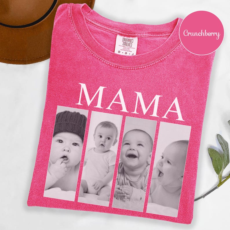 May include: A bright pink short-sleeve t-shirt featuring the word MAMA in white capital letters above four vertical black and white photo panels. Each panel displays a different portrait of an infant. The shirt has a crew neckline and a tag.