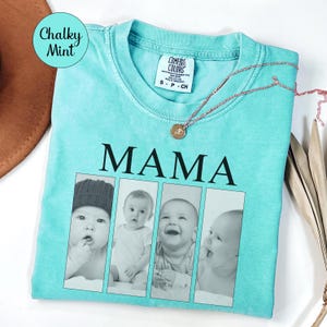 May include: A chalky mint green t-shirt featuring the word MAMA in black capital letters above four vertical rectangular photo frames containing black and white portraits of infants. The shirt has a Comfort Colors label at the inner neckline.