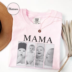 May include: A light pink t-shirt featuring the word MAMA in black capital letters above four vertical black and white photographic panels showing a baby in different poses. A thin gold-toned necklace with a small circular pendant rests on the shirt.