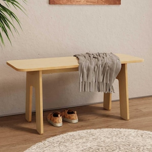 May include: A light wood bench with a gray blanket draped over it. The bench is sitting on a light wood floor with a white rug in front of it.