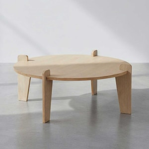 May include: A light-colored, round wooden coffee table with four legs. The table has a simple, modern design, with a smooth surface and a natural wood grain. The table is approximately 18 inches in height and 36 inches in diameter.