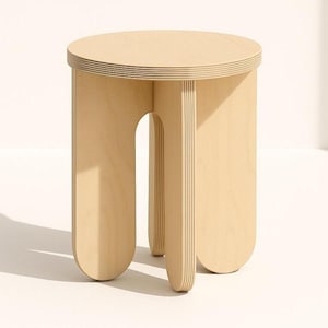 May include: A light-colored wooden stool with a round top and three curved legs. The stool is made of layered wood and has a simple, modern design. The top is approximately 12 inches in diameter.