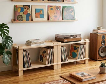 Puede incluir: Dos estantes de pared de madera clara que muestran ocho portadas de discos de vinilo, colocados sobre un mueble multimedia bajo de madera clara que sostiene un tocadiscos y filas de discos de vinilo, con un altavoz de madera cerca.