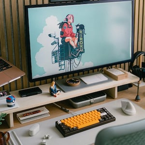 May include: A wooden desk with a computer monitor, keyboard, mouse, and other office supplies. The monitor is displaying an image of an anime character sitting on a building. The desk is also decorated with a small figurine of a person.