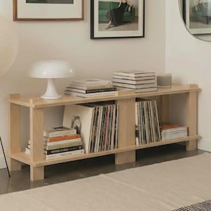May include: A light wood, low-profile media console with open shelving, displaying vinyl records, books, and decorative items. A white paper lantern lamp with an orange accent and a white mushroom-shaped lamp are also visible.