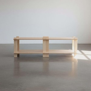 May include: A light-colored wooden bench with two shelves. The bench has a simple, minimalist design with clean lines and a natural wood finish. The bench is approximately 60 inches long, 15 inches wide, and 18 inches tall.