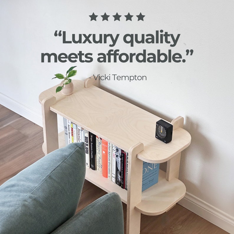 May include: A light-colored wooden bookshelf with rounded edges and multiple shelves. The top shelf holds a small plant and a black clock. The bookshelf is filled with books of various colors. Text on the image reads: "Luxury quality meets affordable."