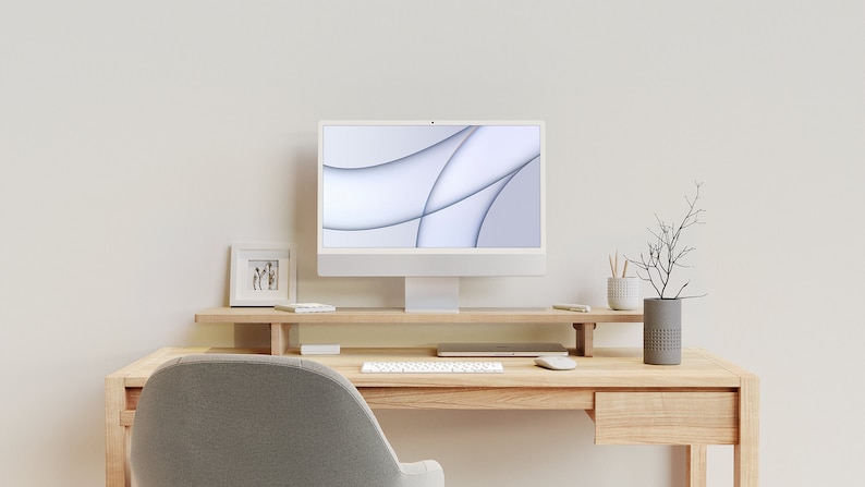 May include: A white computer monitor with a light gray abstract design on the screen sits on a wooden desk with a keyboard, mouse, and a small picture frame. A gray vase with a dried branch sits on the desk.