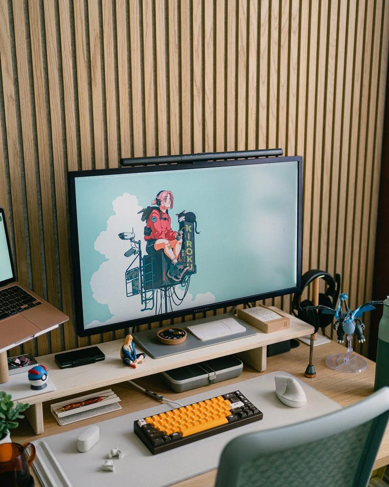 May include: A wooden desk with a computer monitor, keyboard, mouse, and other office supplies. The monitor is displaying an image of an anime character sitting on a building. The desk is also decorated with a small figurine of a person.