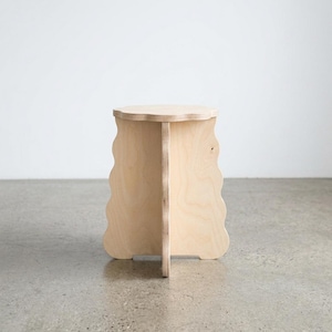 May include: A light-colored wooden stool constructed from plywood with a circular top and a base featuring three vertical panels. The panels have a distinct wavy, scalloped edge design, and the entire structure is assembled with a central joint.