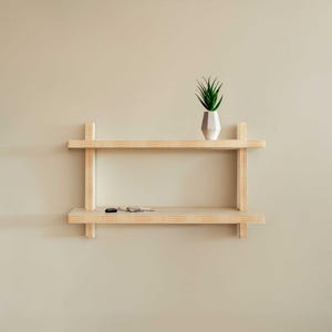 May include: A light wood floating shelf with two shelves. A small potted plant sits on the top shelf.
