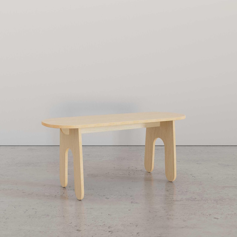 Puede incluir: Un banco de madera clara con la parte superior redondeada y patas curvas &uacute;nicas. El banco est&aacute; sobre un suelo de hormig&oacute;n.