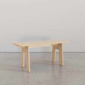 Puede incluir: Una mesa de madera clara con un dise&ntilde;o sencillo. La mesa tiene una tapa rectangular y cuatro patas. Las patas est&aacute;n hechas de una sola pieza de madera que se dobla para formar una forma como una U invertida.