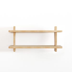 May include: A two-tiered wooden shelf unit with a natural finish. The shelf is mounted to a white wall.