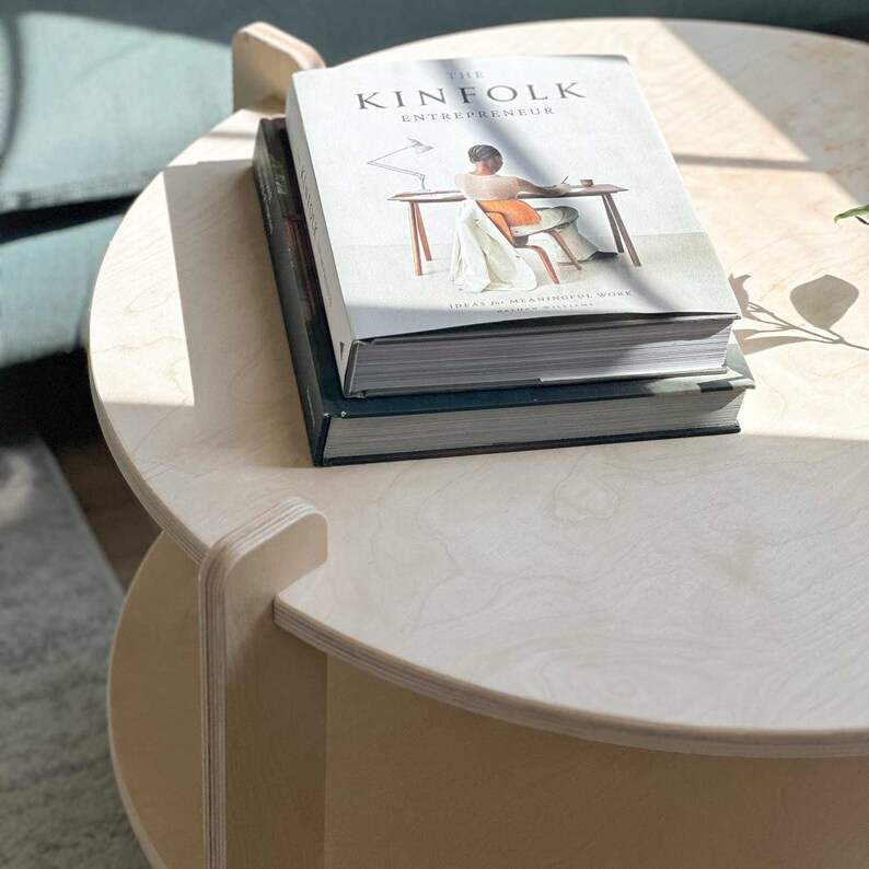 Peut inclure: Une table basse ronde en bois clair avec une &eacute;tag&egrave;re inf&eacute;rieure. Deux livres sont empil&eacute;s sur le dessus de la table. Le livre du dessus est intitul&eacute; "THE KINFOLK ENTREPRENEUR". La table est dans une pi&egrave;ce bien &eacute;clair&eacute;e.