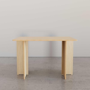 May include: A light-colored wooden table with a rectangular top and four legs. The legs are made of vertical planks that extend to the floor. The table is approximately 48 inches long and 24 inches wide.