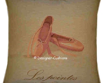 May include: A beige pillow with a tapestry design of two pink ballet shoes. The text "Les pointes" is printed in cursive on the pillow.