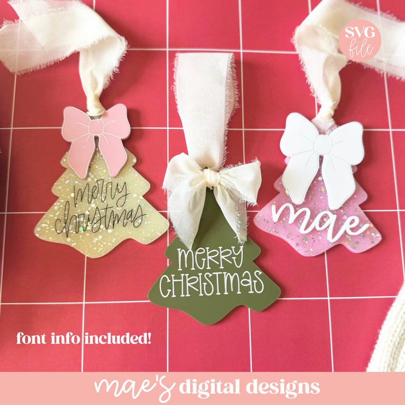May include: Three Christmas tree ornaments with white ribbon and bows. One tree is gold with "Merry Christmas" in script, another is green with the same text, and the last is pink with the name "mae".