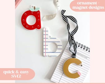 May include: Three wooden alphabet letters, 'a', 'b', and 'c', are displayed. The 'a' is red with apple details, the 'b' is designed like lined paper, and the 'c' is a pencil. The image includes text: 'ornament + magnet designs' and 'mae's digital designs'.