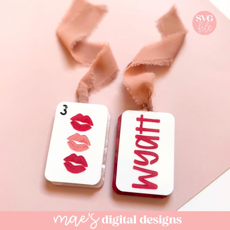 May include: Two white rectangular tags with red accents and pink ribbons. One tag features three red lip illustrations and the number 3. The other tag displays the name "Wyatt" in red. The background is a soft pink.