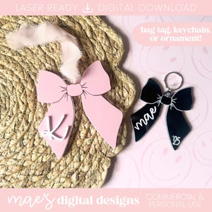 May include: Pink and black bow-shaped bag tags or keychains. One pink bow has a white letter "K" and a ribbon. The black bow keychain has the name "mae" and the number "25". The text "bag tag, keychain, or ornament!" is also visible.