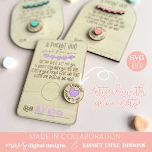Pode incluir: Um cart&atilde;o de madeira com o texto "A Pocket Hug just for you" e um pequeno c&iacute;rculo de madeira com o texto "A Warm Hug From Me To You" com um cora&ccedil;&atilde;o roxo. O cart&atilde;o est&aacute; sobre um fundo rosa com o texto "Attach with glue dots!" e "SVG file".