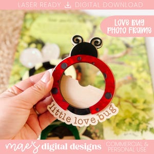Puede incluir: Un marco de fotos de mariquita de madera con un diseño rojo y negro. El marco tiene una abertura circular y las palabras "little love bug" están escritas en la parte inferior. El texto "LOVE BUG PHOTO FRAME" también es visible.
