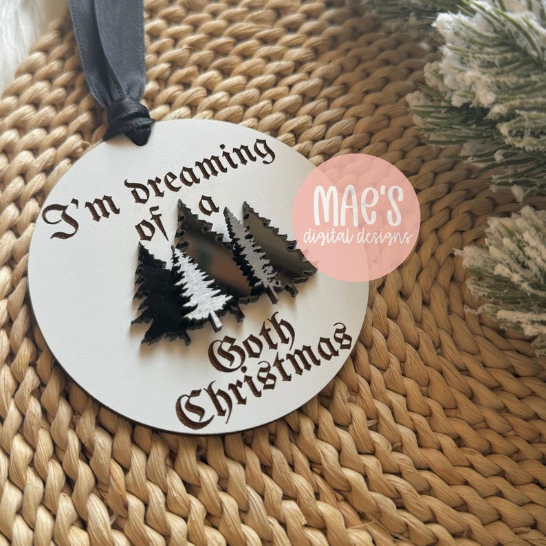 May include: White round wooden ornament with black text that reads "I'm dreaming of a Goth Christmas" and three black and white stylized Christmas trees.