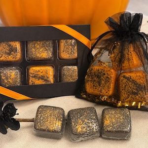 May include: A black rectangular box with a window containing six square orange and black speckled items, a black organza drawstring bag holding three similar square items, and three additional square items placed in front.