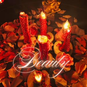 Op de afbeelding: Een romantisch stilleven met drie rode kaarsen met flikkerende vlammen, omringd door rozenblaadjes en schijfjes fruit. Het woord "Beauty" is in een gloeiend schrift over de scène geschreven, met een gouden beeld in de achtergrond.