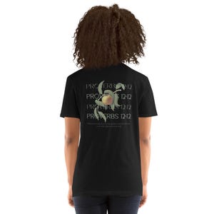 May include: Black t-shirt featuring a graphic of a peach and the text "PROVERBS 12:12" repeated five times. The text is in a white, serif font.