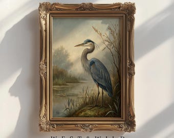 May include: A framed painting of a Great Blue Heron standing near a body of water. The artwork is in a gold ornate frame. The painting has a muted color palette with the text "AVAILABLE IN PRINT & FRAMED OPTIONS" at the top and "WEST & WILD" at the bottom.