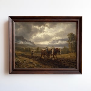 May include: A framed landscape painting depicts a farmer plowing a field with two horses. The artwork features a dark, wooden frame and a dramatic sky with mountains in the background. The color palette is dominated by earthy tones.