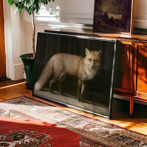 May include: A framed artwork featuring a detailed painting of a fox. The fox has a light brown coat and is standing against a dark background. The artwork is displayed on a wooden floor, leaning against a cabinet, with a red rug in the foreground.