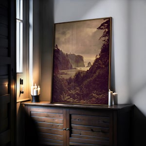 May include: A framed landscape art print depicting a coastal scene with cliffs, trees, and a cloudy sky. The artwork is displayed on a dark wooden cabinet, with candles and a window in the background. The frame is gold-colored.