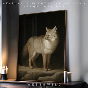 May include: A framed artwork featuring a detailed painting of a fox in shades of tan and cream, set against a dark background. The artwork is displayed on a wooden surface, with text at the top reading "AVAILABLE IN PHYSICAL PRINTS & FRAMED OPTIONS" and the brand name "WEST & WILD" at the bottom.
