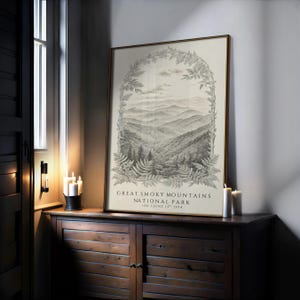 May include: A framed print of the Great Smoky Mountains National Park. The black and white landscape art features a mountain range and fern border. The text reads "Great Smoky Mountains National Park, Est. June 15th 1934."