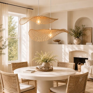 Può includere: Due ampie lampade a sospensione con bordi ondulati realizzate in rattan intrecciato color marrone chiaro pendono da cavi bianchi. Ogni apparecchio presenta una lampadina a vista centrata nella struttura a griglia aperta.