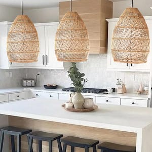 May include: A white kitchen island with a white worktop and four black wooden stools. Three wicker pendant lights hang above the island.