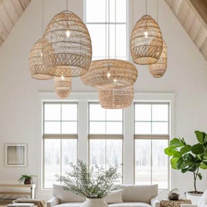 May include: A spacious living room with several woven rattan pendant lights suspended from a high, vaulted ceiling. The lights are different sizes and shapes. The room includes white sofas, a wooden coffee table, and large windows.