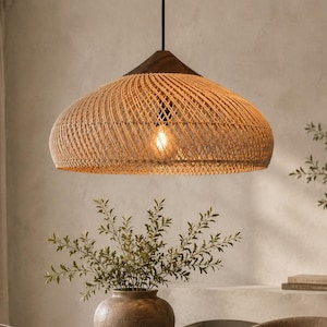 May include: A dome-shaped pendant light fitting featuring a woven rattan shade with a natural tan finish and a dark brown wooden top cap. The light hangs from a black cord and contains a single visible light bulb emitting a warm glow.