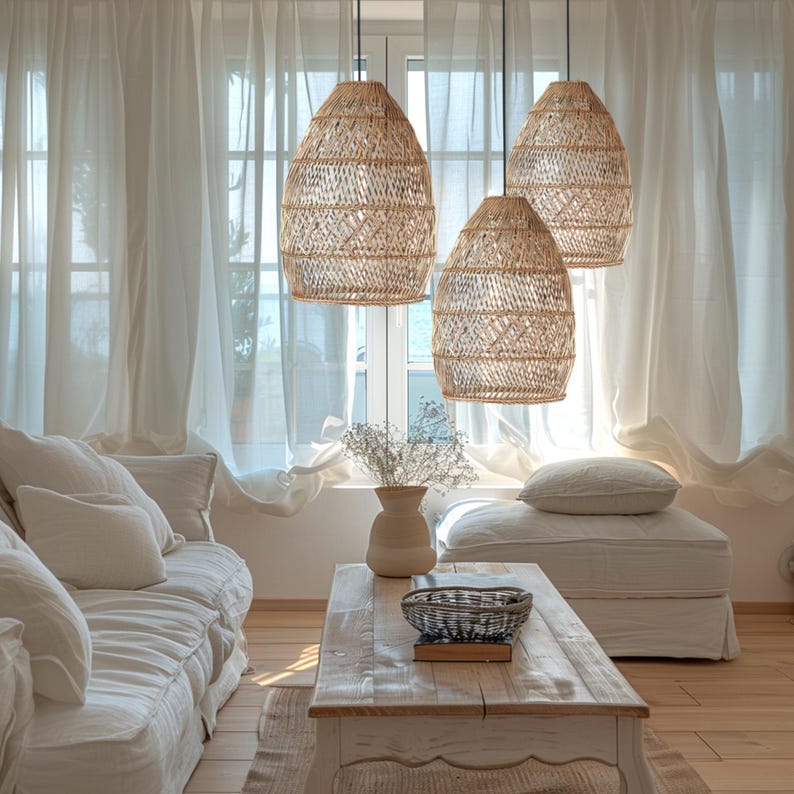 May include: Three woven wicker pendant lights hang from the ceiling in a living room with white curtains and a white sofa. The lights are a natural beige colour and have a geometric pattern.