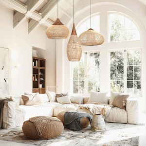 K&ouml;nnte beinhalten: Drei gewebte Pendelleuchten mit Holzaufs&auml;tzen h&auml;ngen &uuml;ber einem cremefarbenen Ecksofa. Der Raum verf&uuml;gt &uuml;ber gro&szlig;e Fenster, einen gemusterten Teppich und gewebte Ottomanen, die einen warmen und einladenden Wohnraum schaffen. Die Leuchten sind aus nat&uuml;rlichen Materialien.