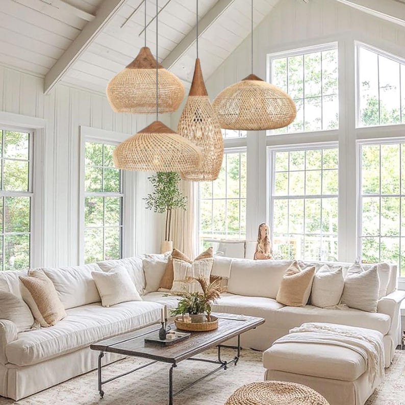 K&ouml;nnte beinhalten: Ein helles Wohnzimmer mit vier gewebten Pendelleuchten mit Holzaufs&auml;tzen. Die Leuchten h&auml;ngen &uuml;ber einem wei&szlig;en Ecksofa mit beigen Kissen. Ein Couchtisch und eine Ottomane aus Holz vervollst&auml;ndigen den Raum in neutralen T&ouml;nen.