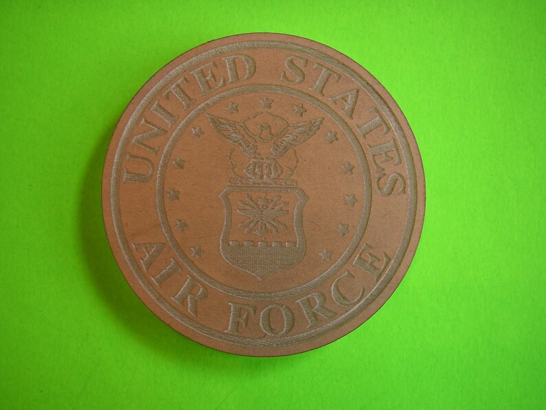 May include: A brown wooden coaster with the United States Air Force seal. The seal features a bald eagle with wings spread, a shield with stars, and the words "United States Air Force".