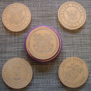 May include: Five round coasters with the seals of the United States Army, Navy, Coast Guard, Air Force, and Marine Corps. Each coaster is made of a light brown material and has a raised edge.
