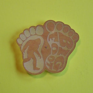 May include: A wooden cutout of two bare feet with the word "Free" written on one foot and the word "Feet" written on the other foot.